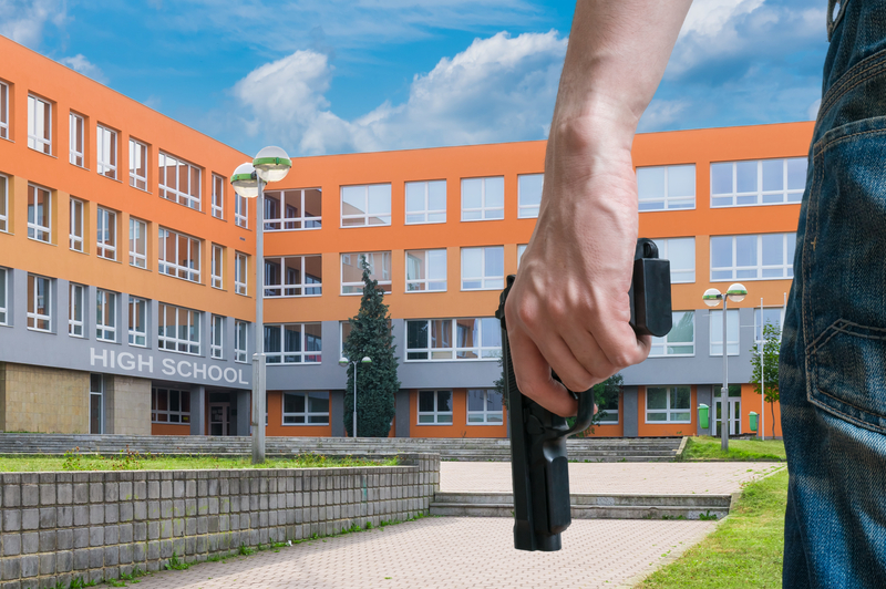 student holding a pistol in front of a school